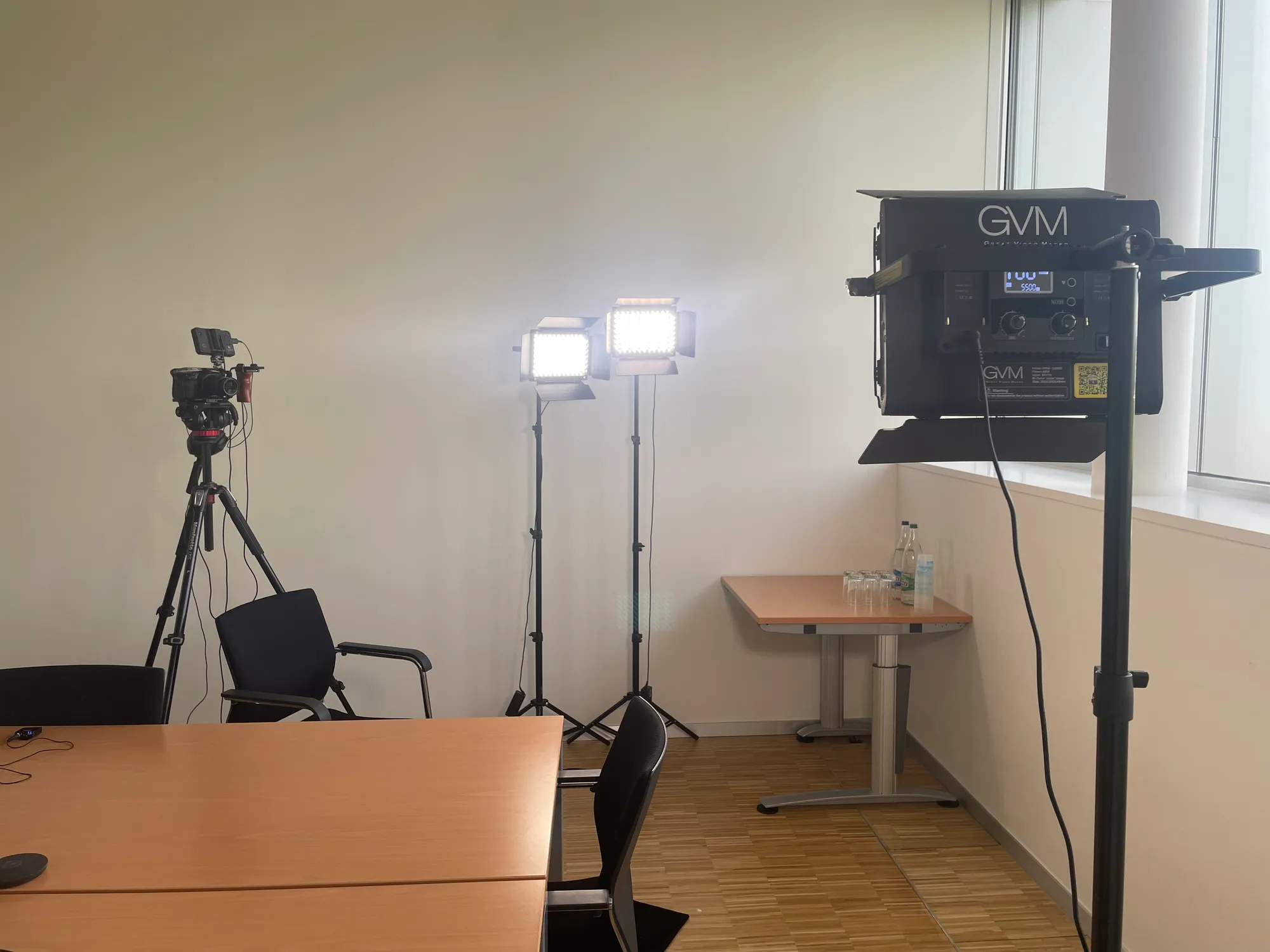 A room prepared for an interview: camera on a tripod, lights switched on, table and chairs still empty.