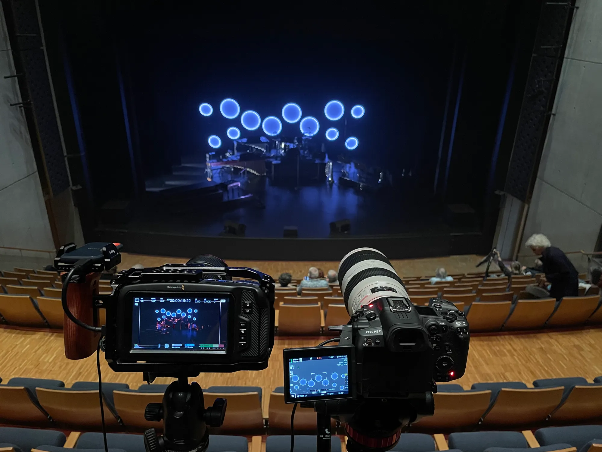 Two cameras set up in the seating, facing the lit stage.